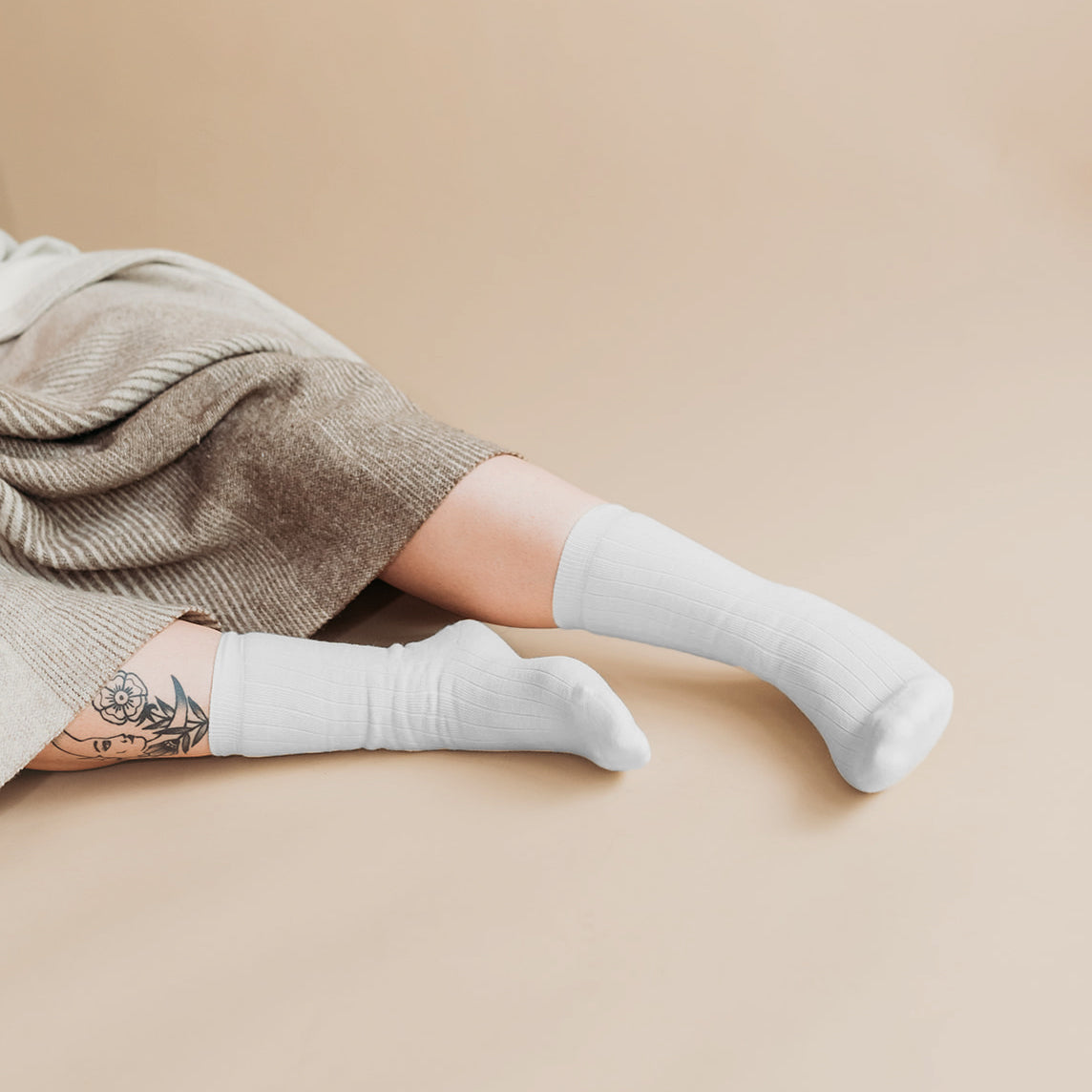 Person lying down wearing white ribbed knee-high organic cotton socks with floral leg tattoo | Q for Quinn