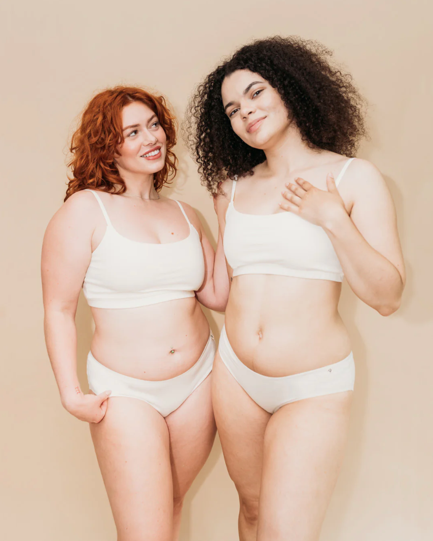 Two women wearing white lingerie against a beige background