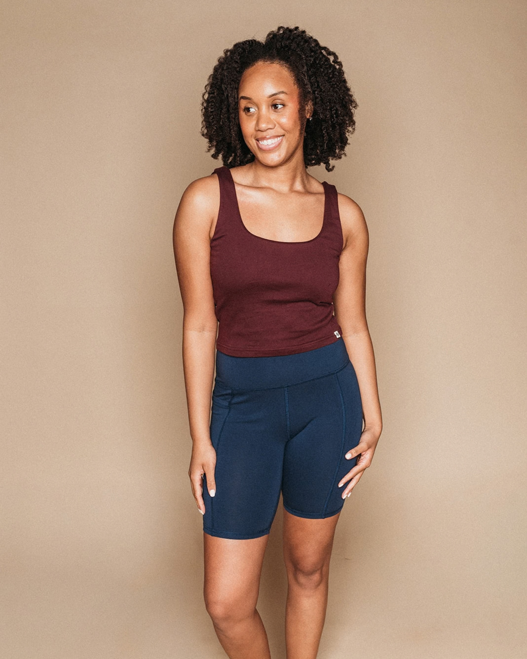 Woman wearing a maroon organic cotton tank top and navy blue shorts against a beige background