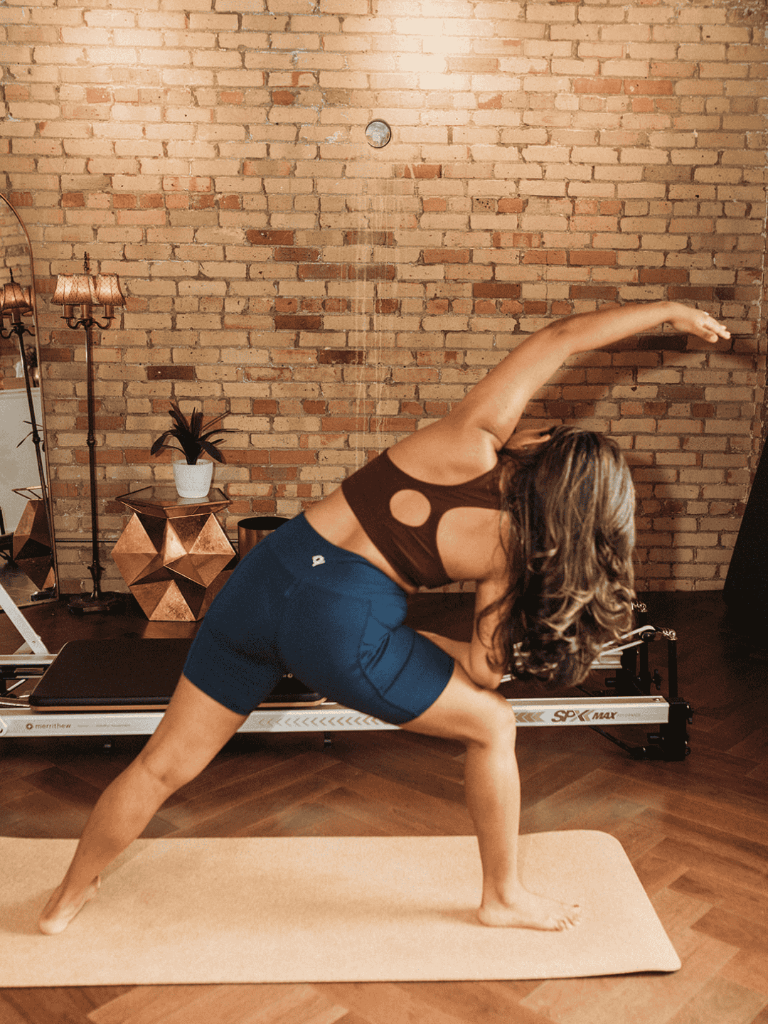Woman practicing yoga in a studio with brick wall and equipment in the background