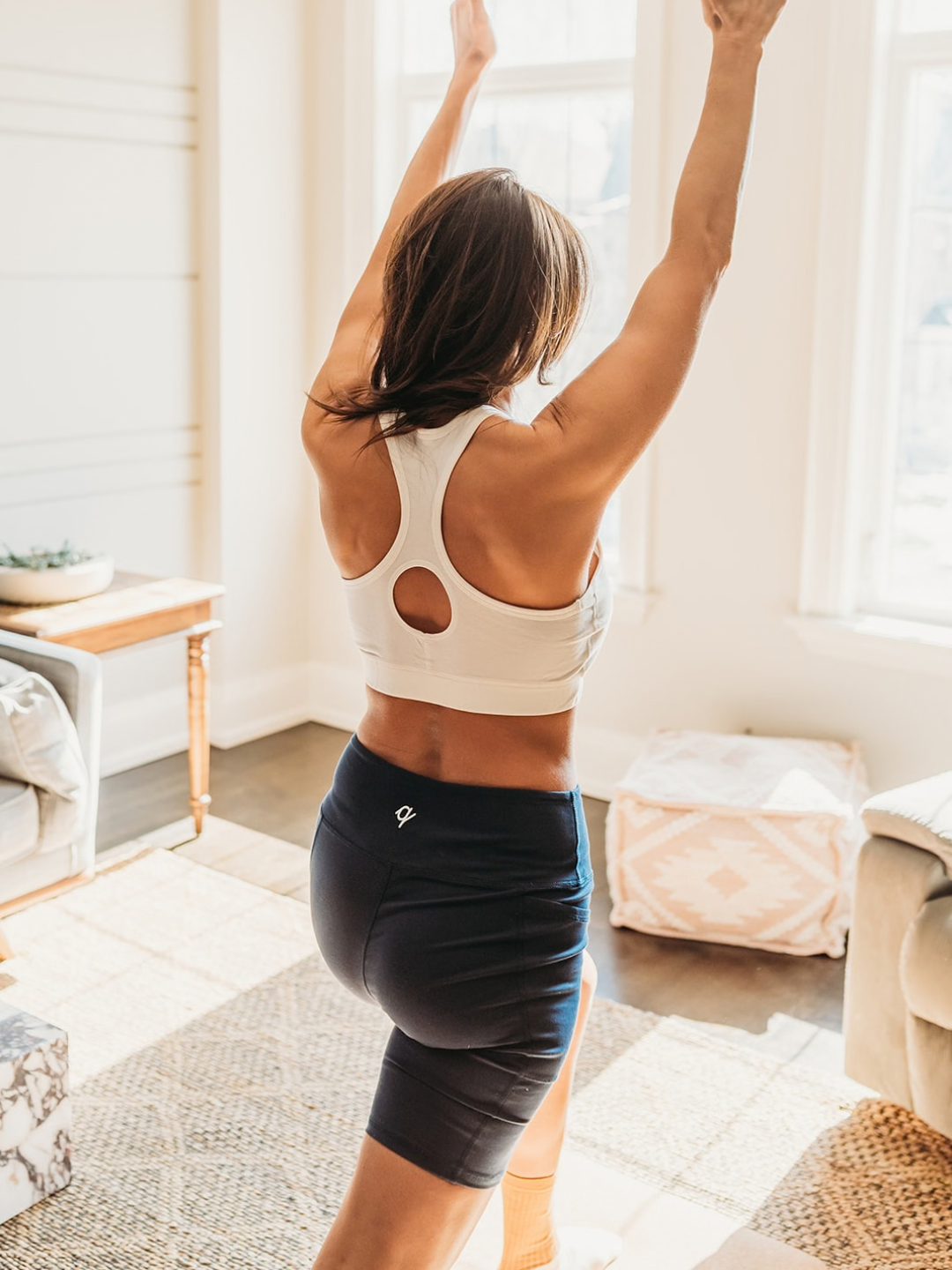 Woman in athletic wear stretching in a bright living room.
