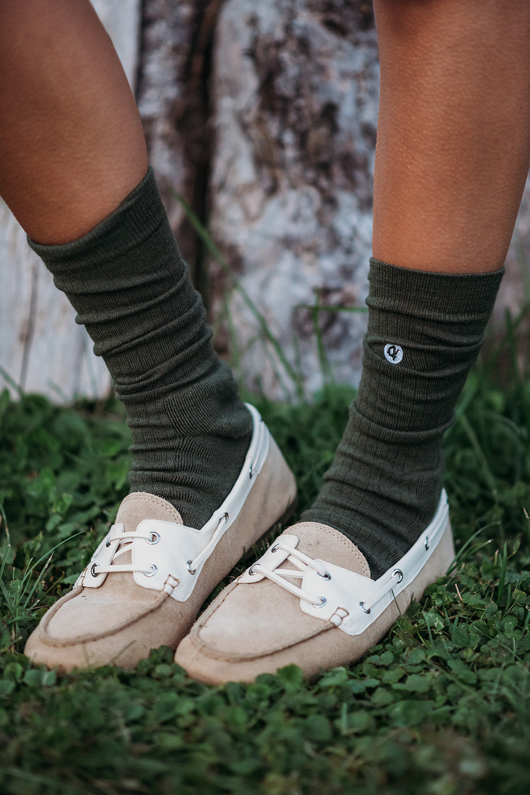 Person wearing dark green socks and beige loafers on grass