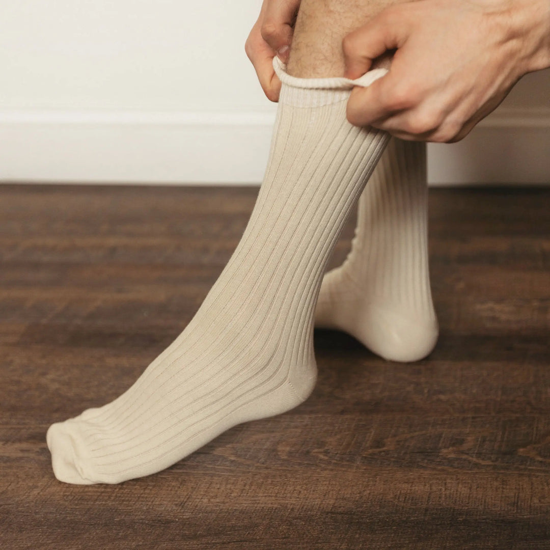 Person pulling on Pure ribbed organic cotton adult socks in natural cream color on wood floor | Q for Quinn