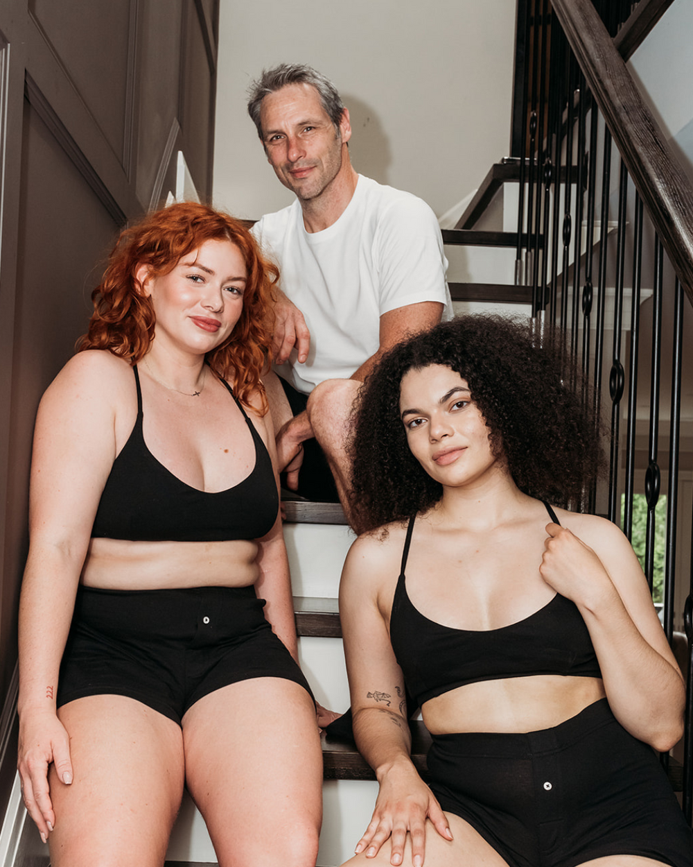 Two women seated on stairs and a man standing wearing Everyday Knit Organic Cotton Boxers in Black | Q for Quinn