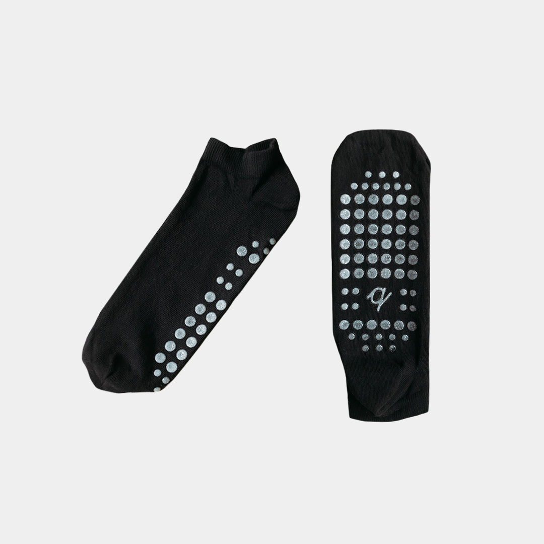 A pair of black low-cut socks with silver grip dots on the sole and heel, displayed against a light gray background.