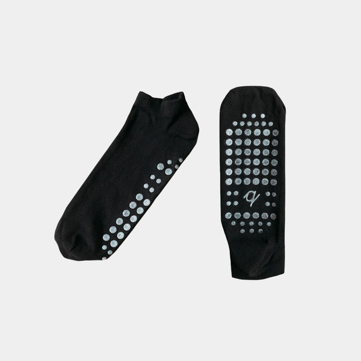 A pair of black low-cut socks with silver grip dots on the sole and heel, displayed against a light gray background.
