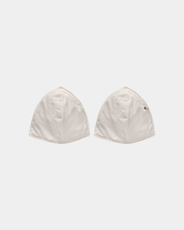 Two off-white cotton capes with a small black embroidered logo on the right cape, displayed side-by-side on a light gray background.