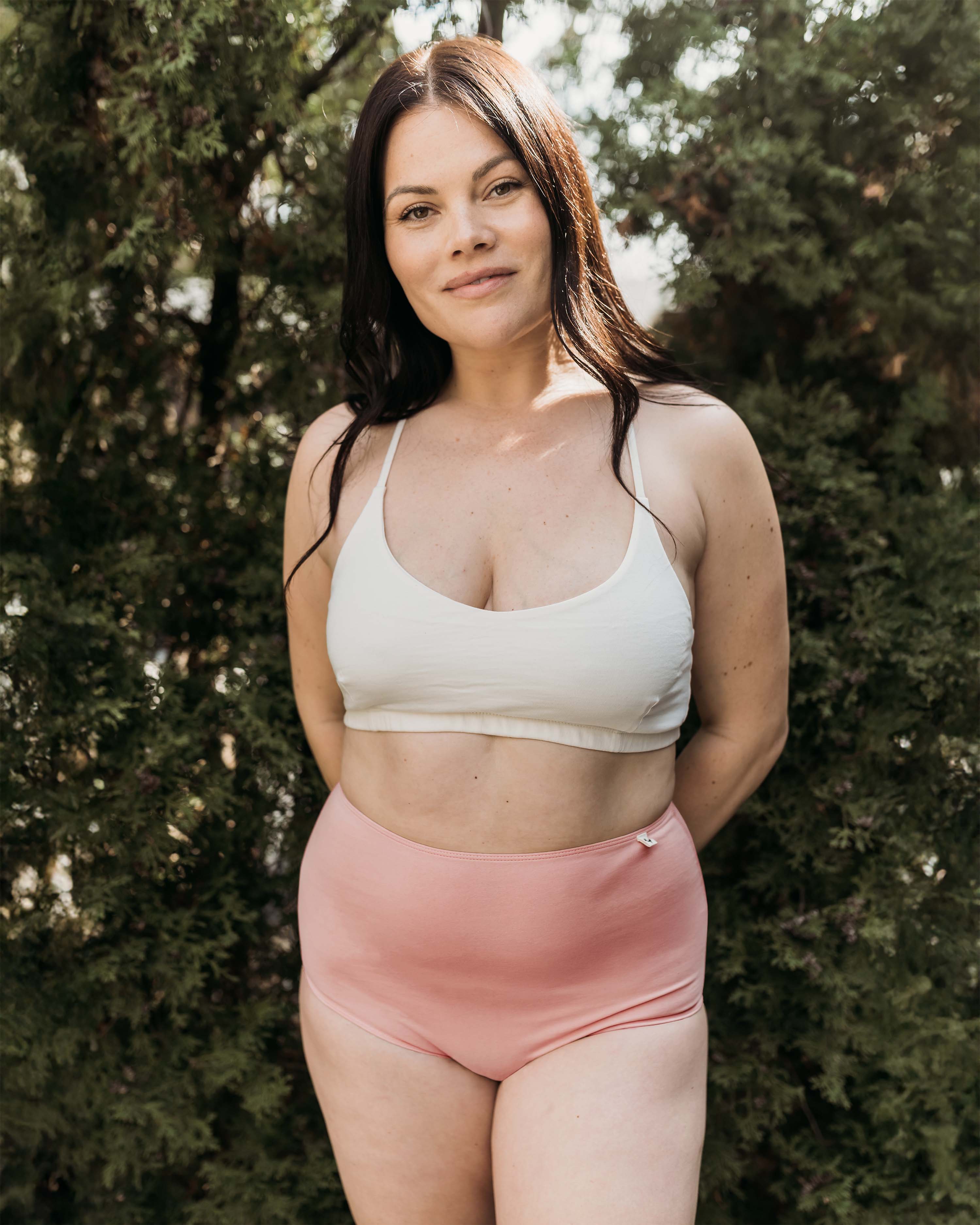 Model outdoors in Women's High Waist Brief in Light Madder with white organic cotton bralette, trees in back | Q for Quinn