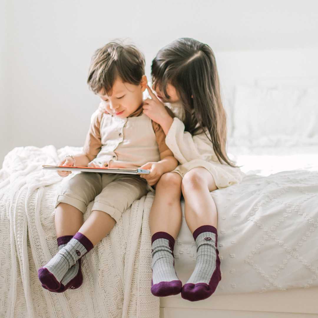 A boy reading a book with sister wearing merino wool socks 