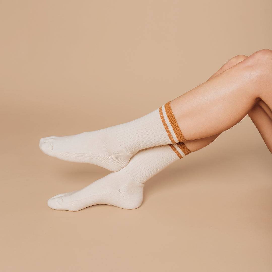 White socks with brown trim worn by a person on a beige background