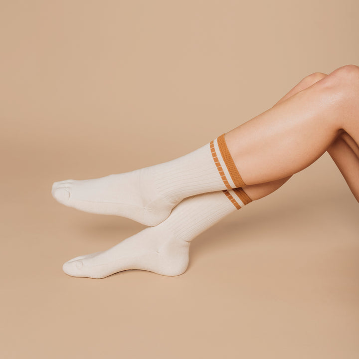 White socks with brown trim worn by a person on a beige background