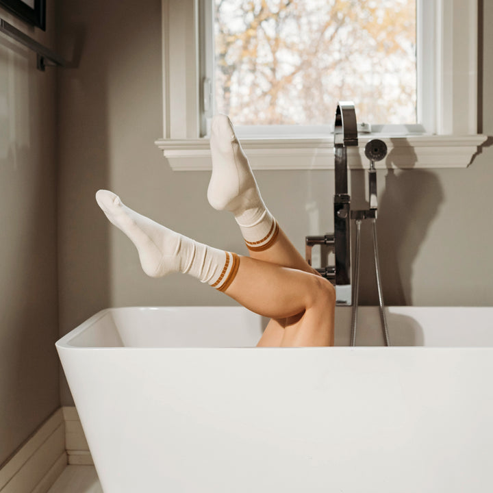Person with feet up in a bathtub in a bathroom with a window in the background