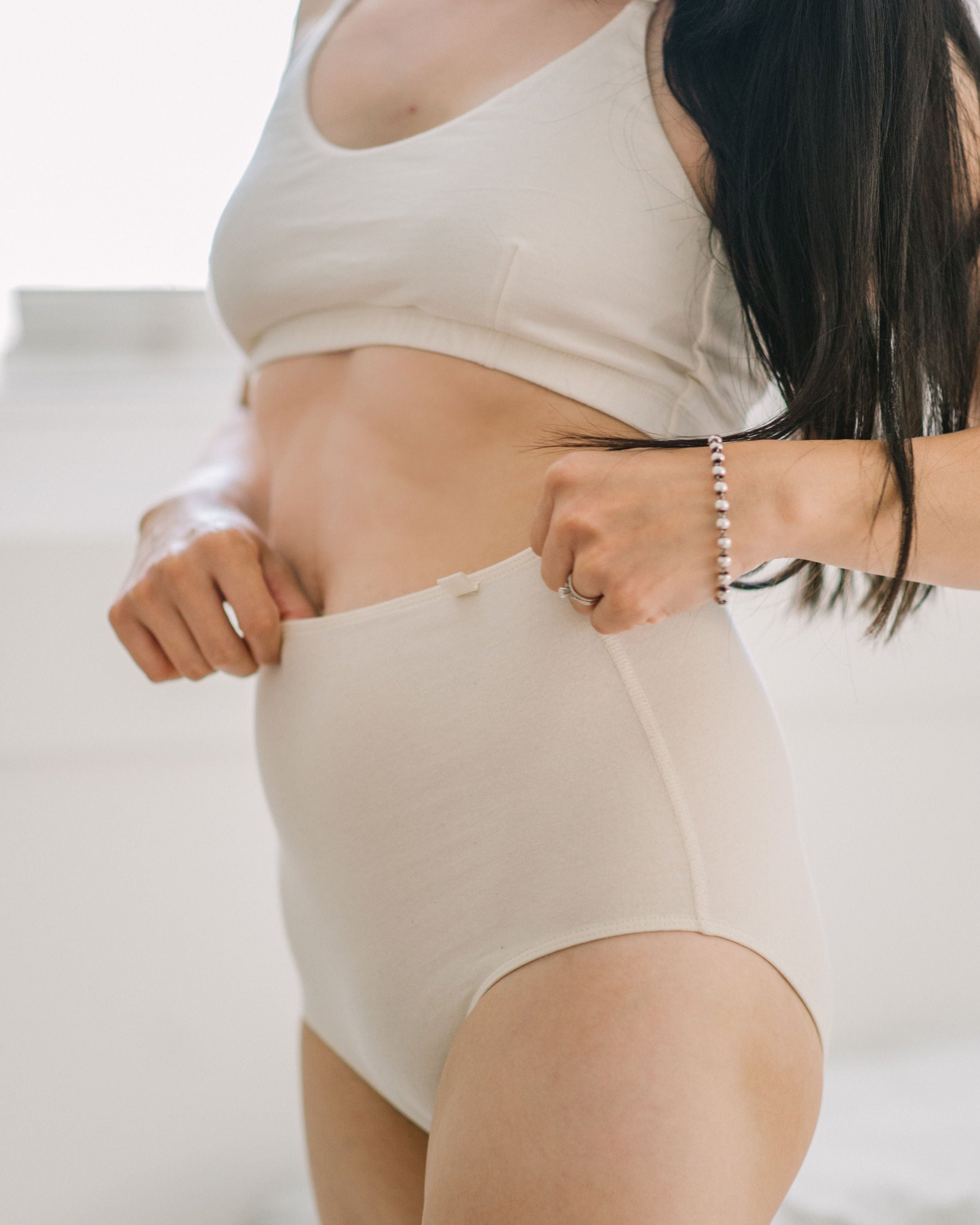 Woman in high-waist beige organic cotton brief underwear, pulling up waistband | Q for Quinn