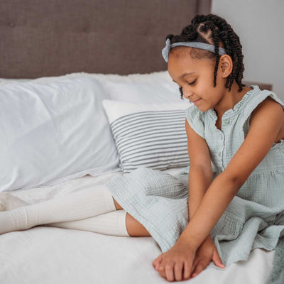 A Girl Sitting in Bed Wears Ribbed Knee High Socks From QforQuinn