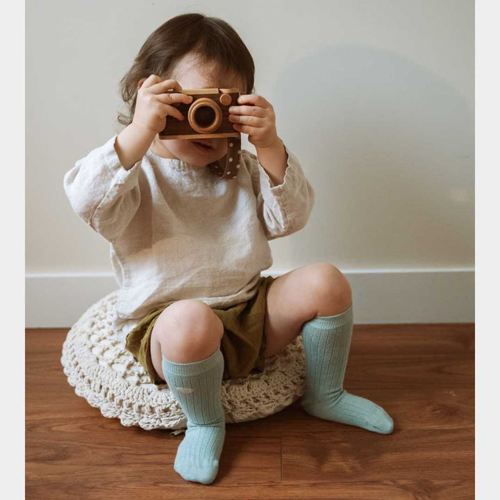 A little girl play with camera and wears organic cotton knee high socks 