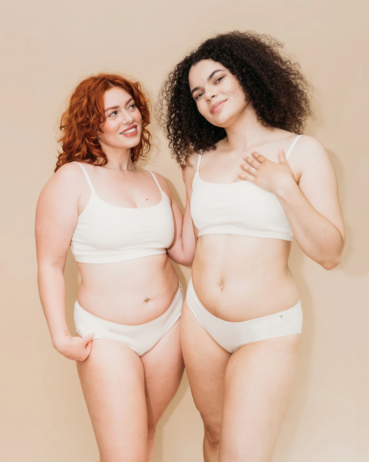 Two women wearing white lingerie against a beige background
