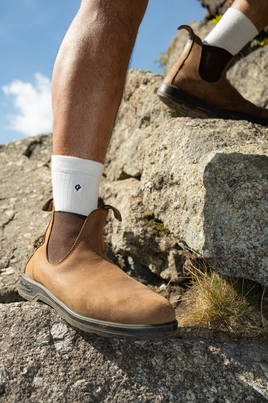 Person wearing white Q for Quinn socks and boots, walking up a cliff