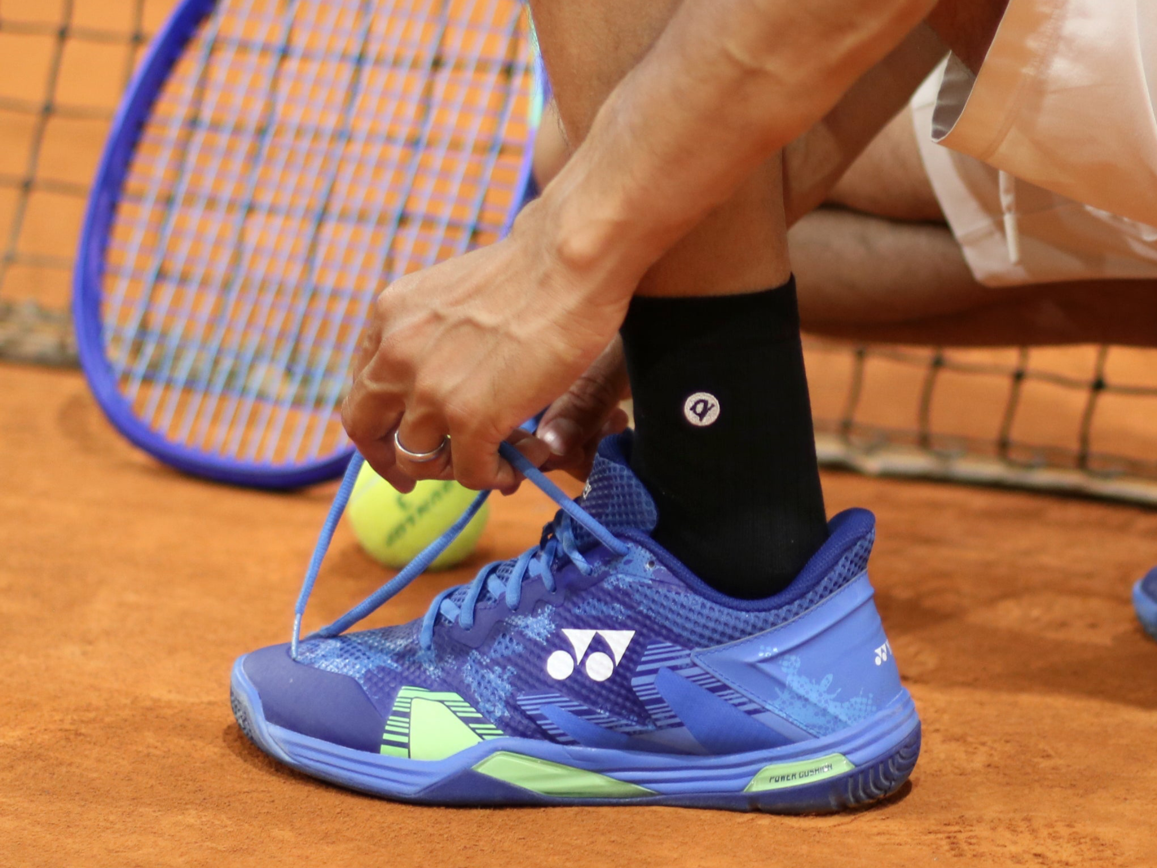 Person tying blue athletic shoes on a tennis court with a racket and ball in the background.