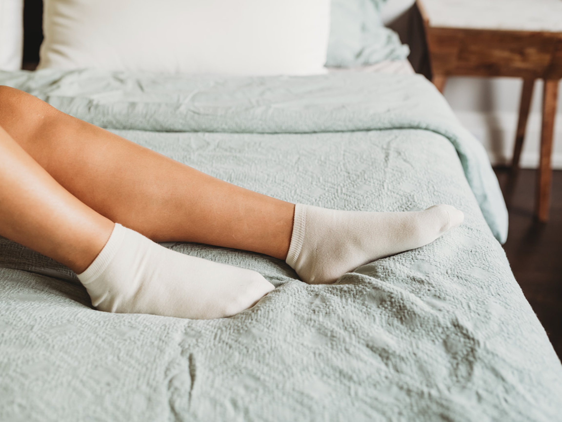 Person wearing white socks on a bed with light green bedding