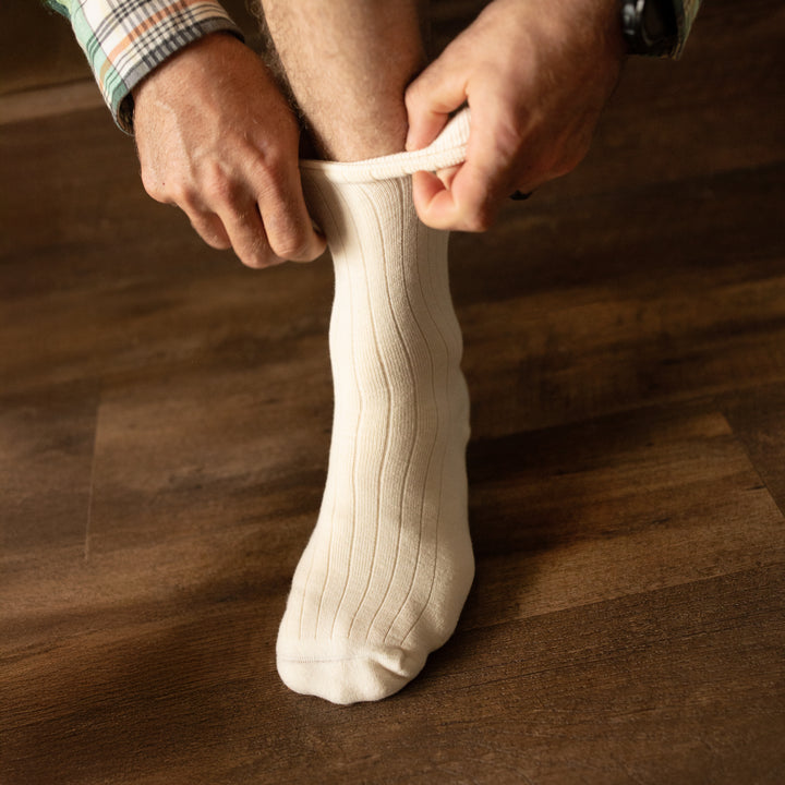 Person pulling on Pure (no dye) Heavyweight Organic Cotton Adult Socks onto foot on wood floor | Q for Quinn