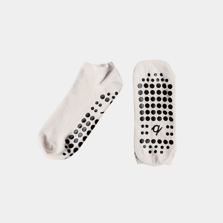 A pair of low-cut white socks with black grip dots on the sole and heel, displayed against a light gray background.