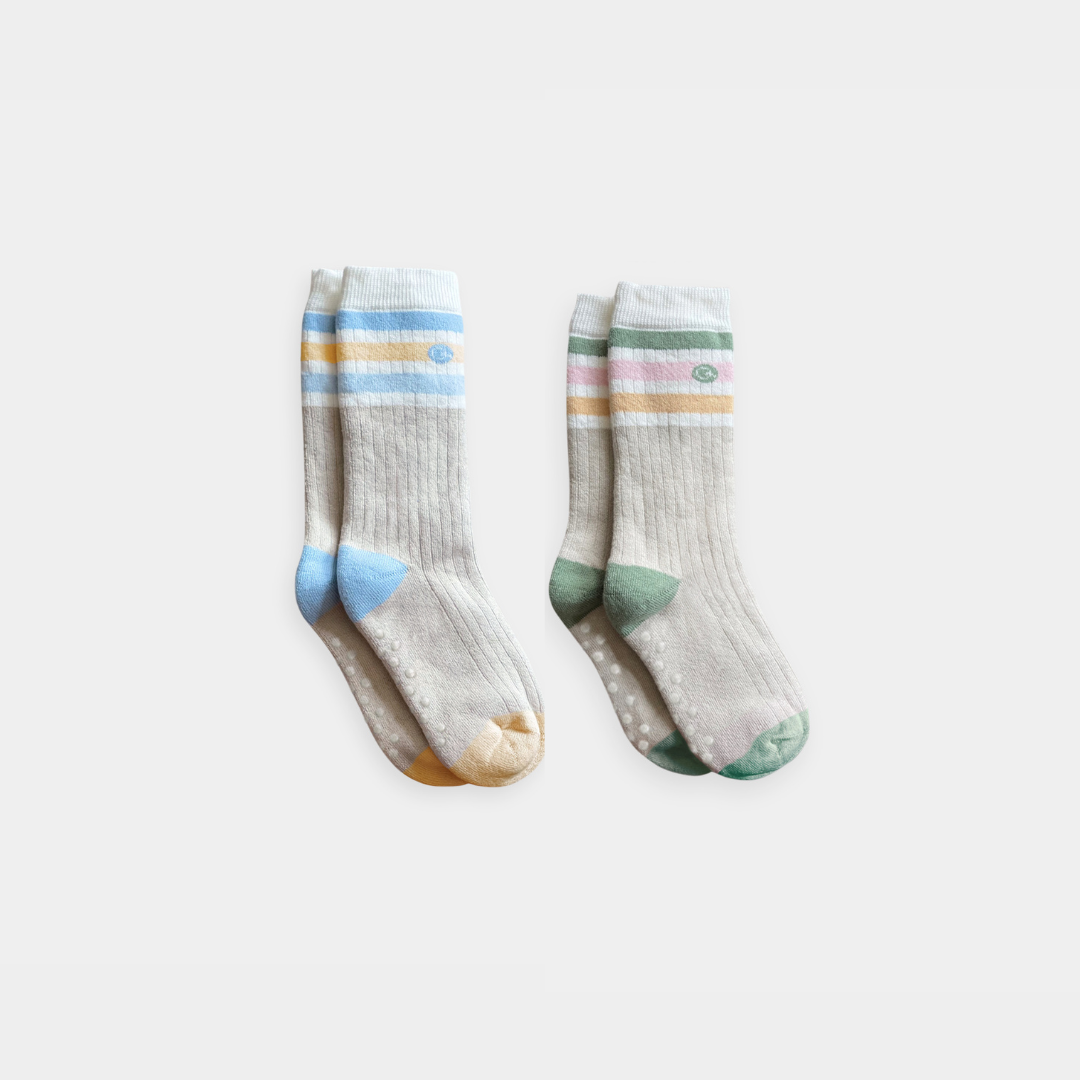 Two pairs of ribbed baby socks with pastel stripes and grip dots, displayed on a clean light gray background.