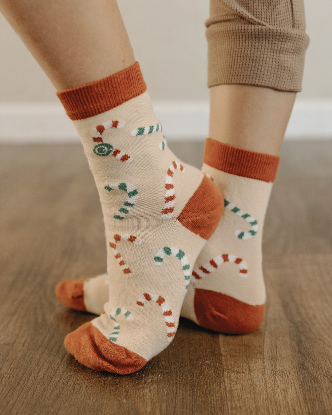 Person wearing patterned socks with orange and beige tones on a wooden floor.