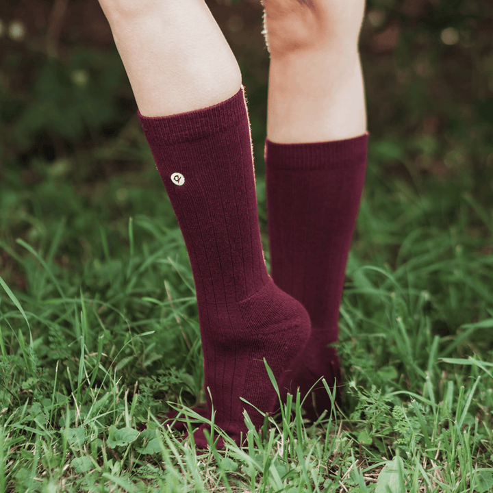 A close-up of a person's legs wearing ribbed knee-high maroon socks standing in green grass outdoors.