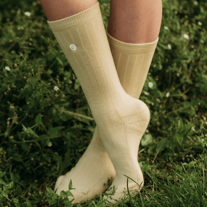 A close-up of a person's legs wearing cream-colored ribbed crew socks standing in green grass.