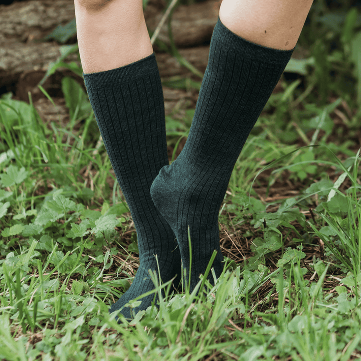 A close-up of a person's legs wearing dark charcoal gray ribbed knee-high socks, standing outdoors in green grass and foliage.