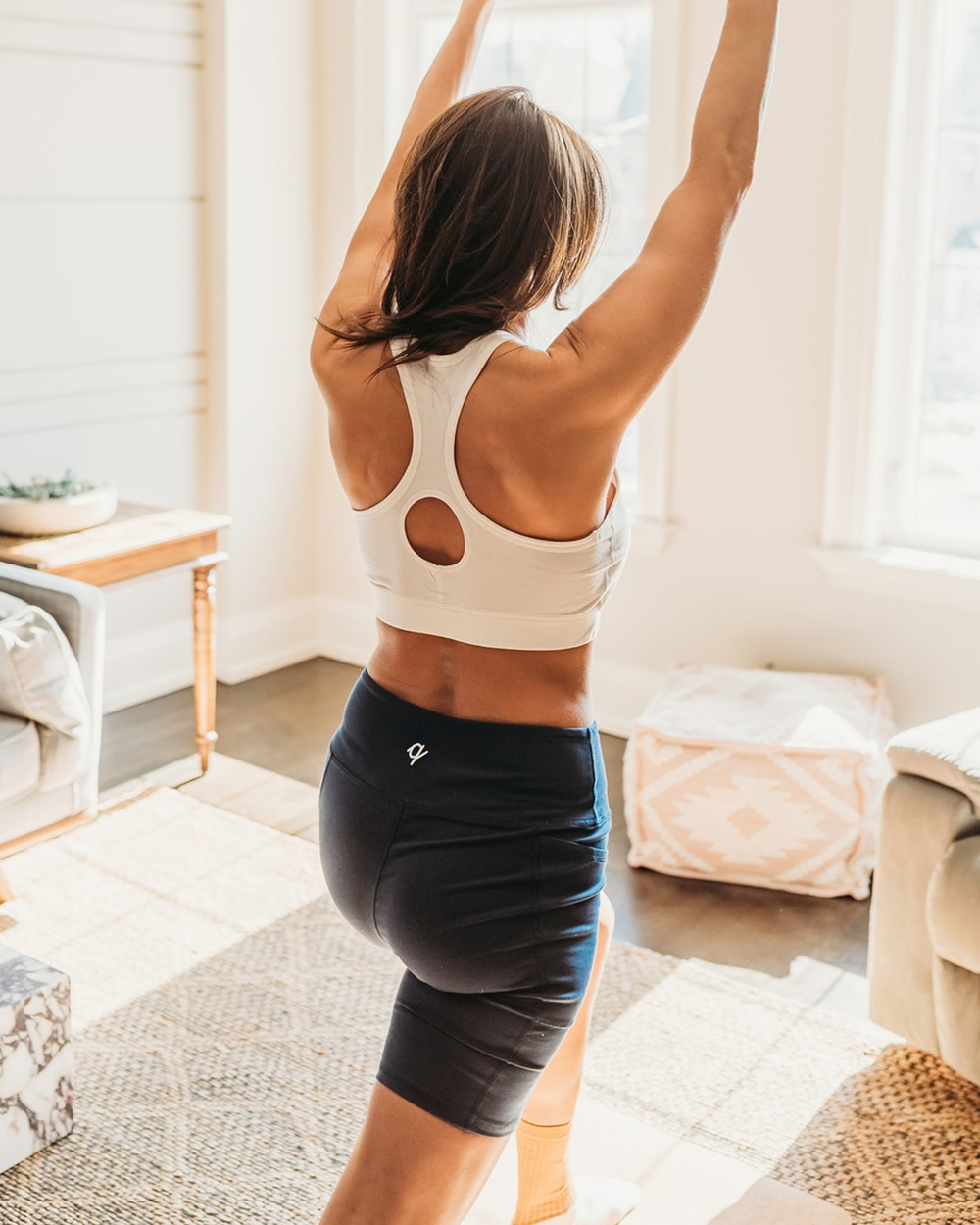 Woman in athletic wear stretching in a bright living room.