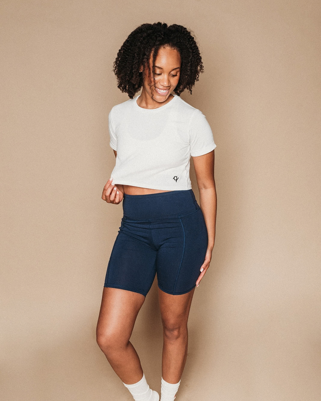 Woman wearing a white crop top and navy shorts on a beige background