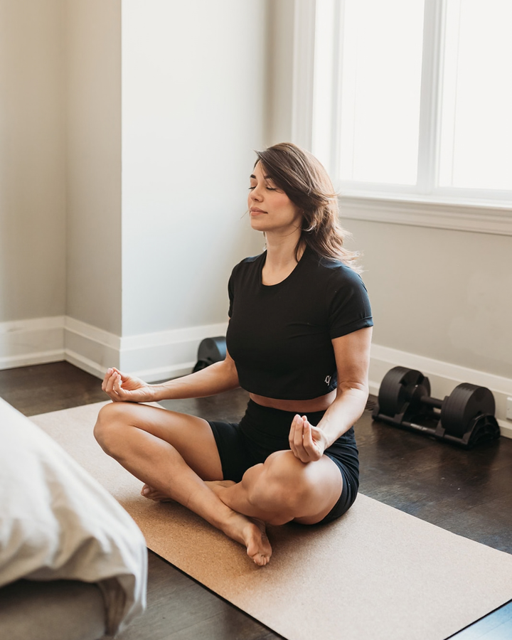 Woman practicing yoga in a room with windows and exercise equipment.