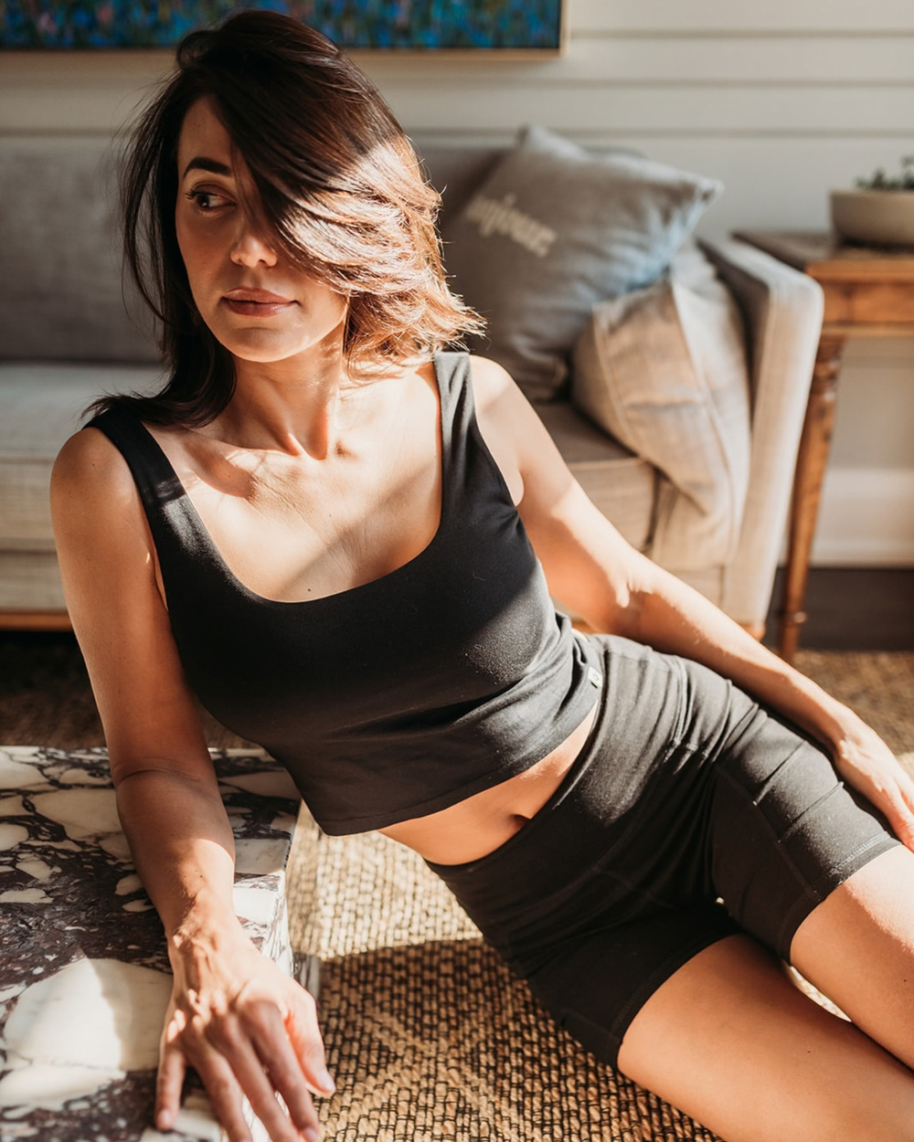 Woman in black athletic wear sitting on a textured surface with a blurred indoor background