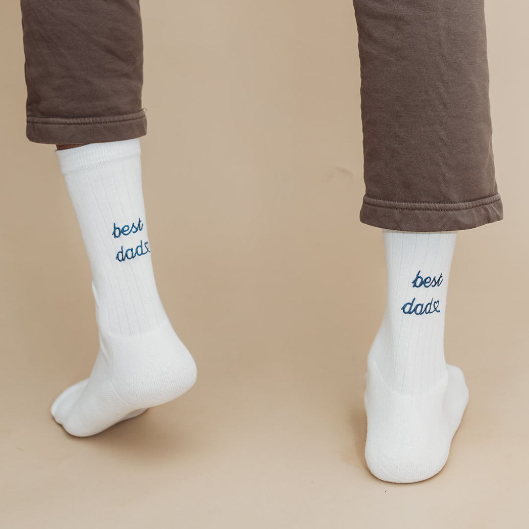 White socks with 'best dad' text worn by a person on a beige background