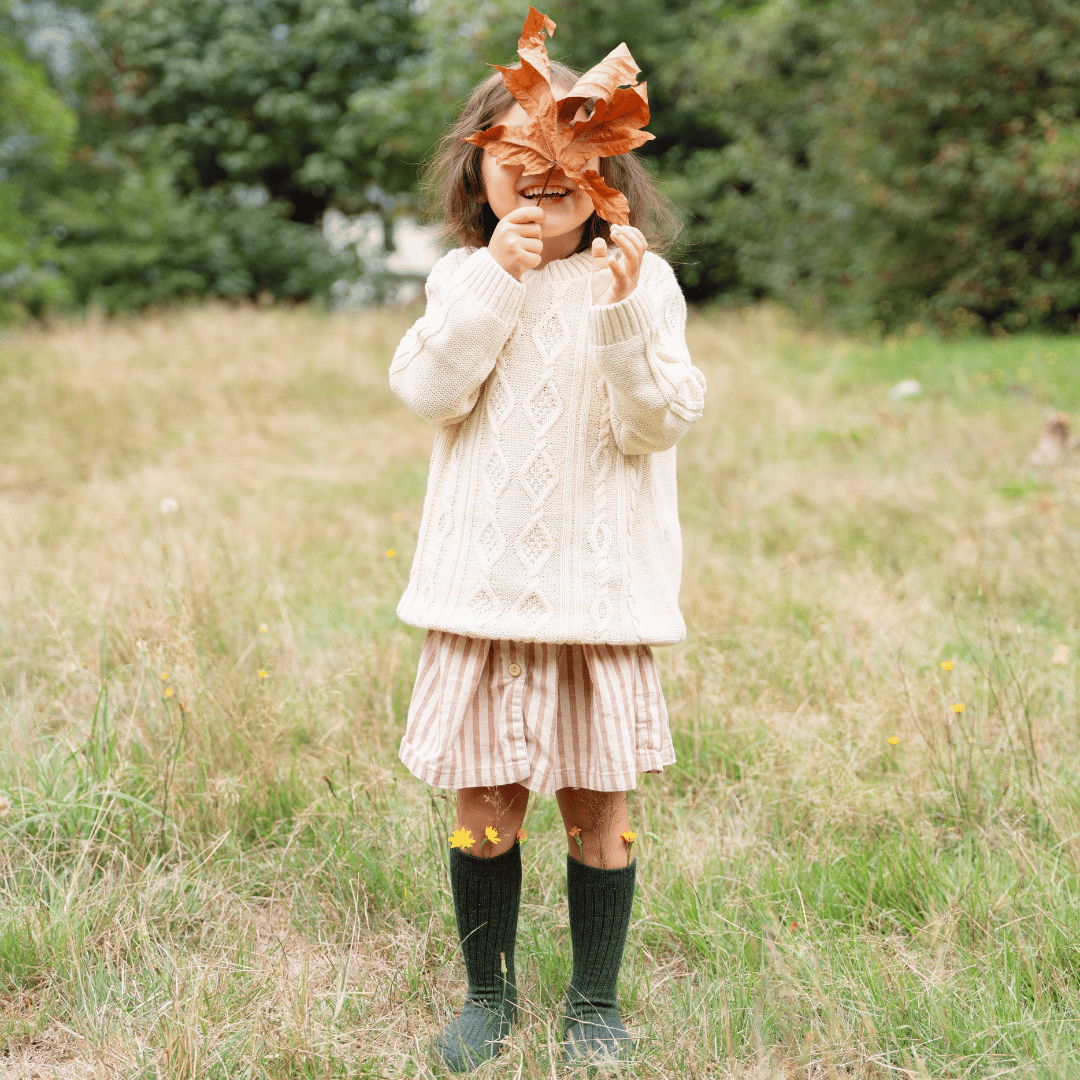 child holding up a leaf in front of her face and wearing green merino wool socks