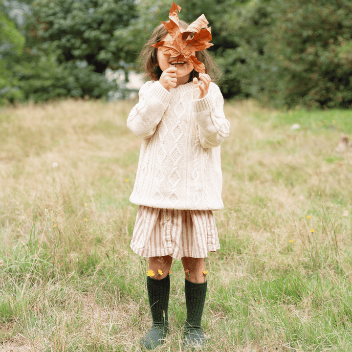child holding up a leaf in front of her face and wearing green merino wool socks