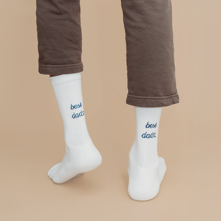 White socks with 'best dad' text worn by a person in brown pants on a beige background