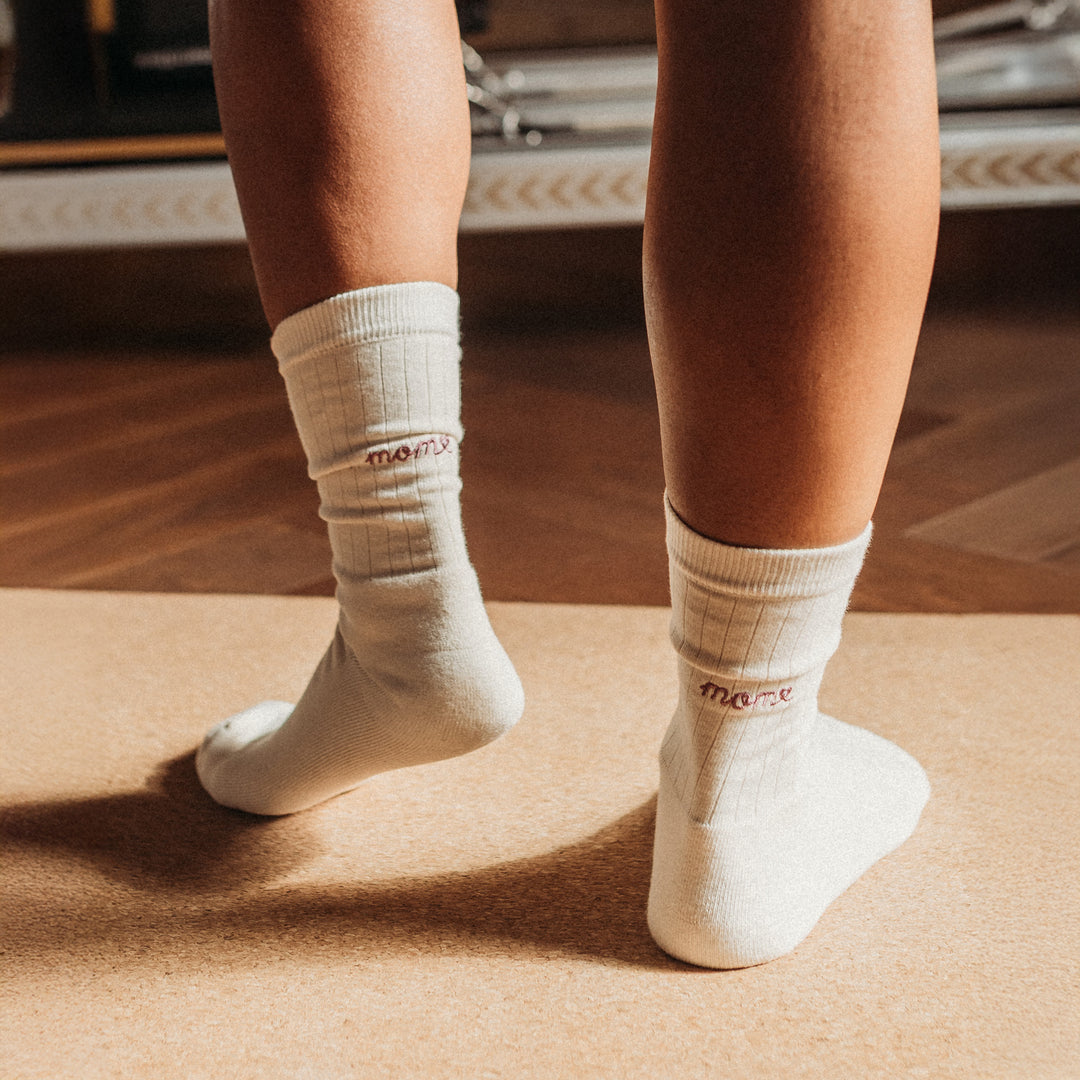 White socks with brand logo worn by a person on a wooden floor.
