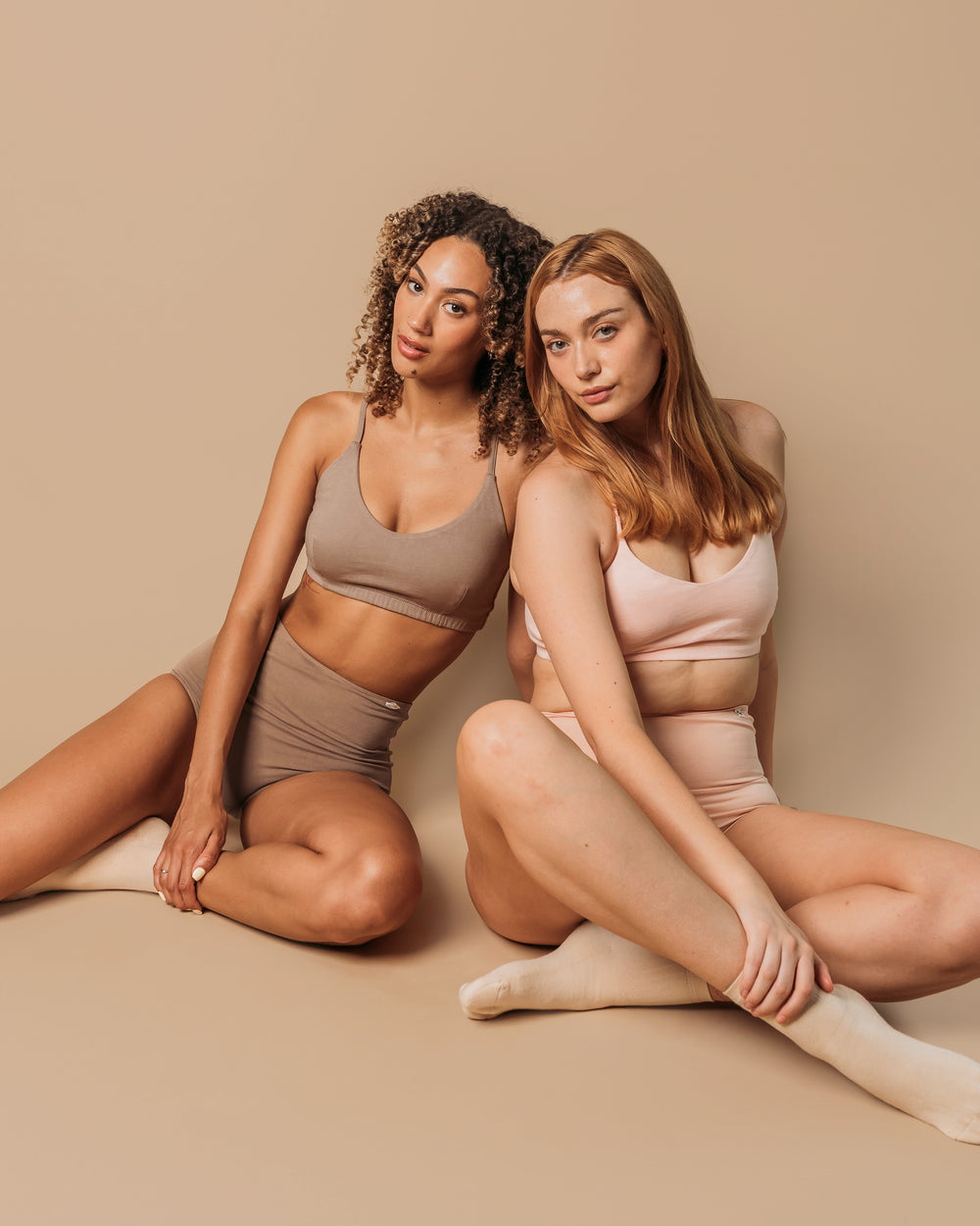 Two women sitting in Women's Criss-Cross Bralettes in Dark Nude and Lilac with matching organic cotton briefs | Q for Quinn