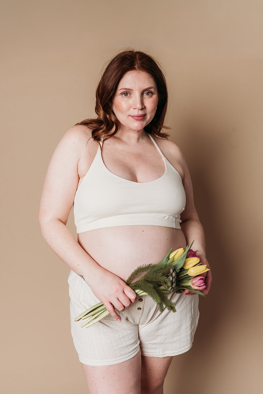 Pregnant woman holding flowers against a beige background