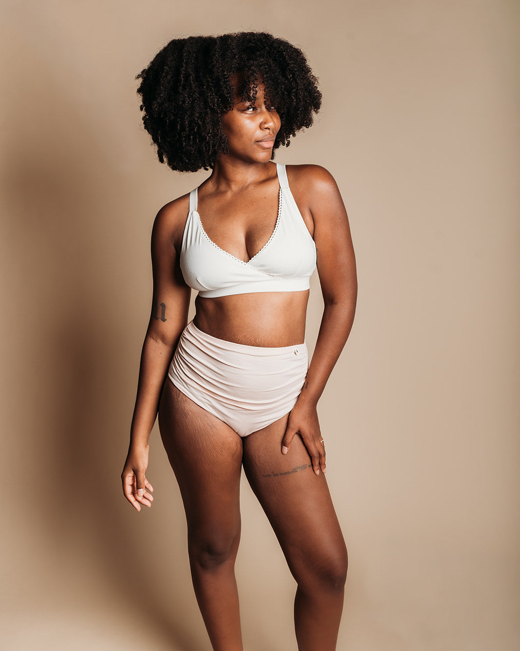 A woman modeling a white two-piece bikini set with matching white socks against a solid beige studio background.